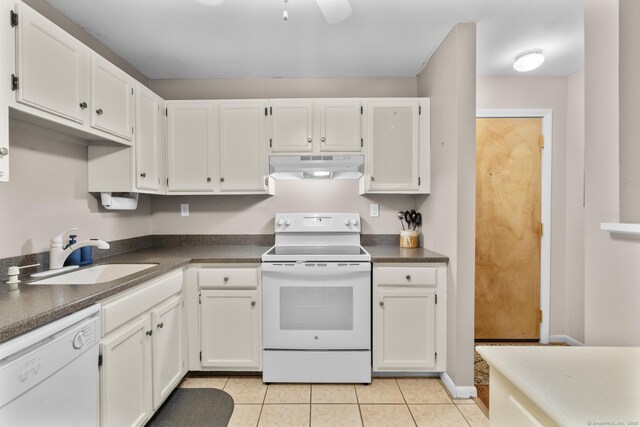 kitchen featuring light tile patterned flooring, dark countertops, white appliances, under cabinet range hood, and a sink