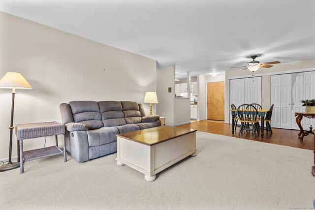 living area with baseboards, ceiling fan, carpet flooring, and wood finished floors