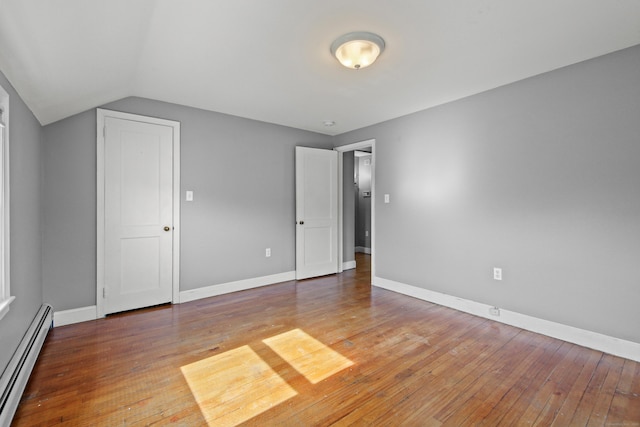 unfurnished bedroom featuring baseboards, baseboard heating, lofted ceiling, and light wood-style floors