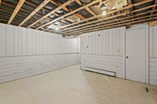 finished below grade area featuring wood walls, light floors, and a baseboard heating unit