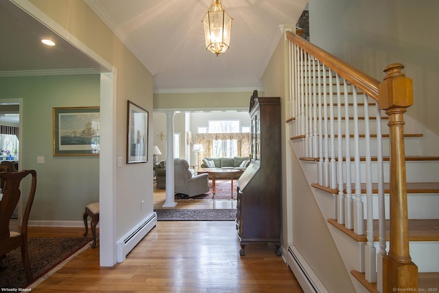 foyer entrance with ornamental molding, stairway, baseboard heating, and wood finished floors