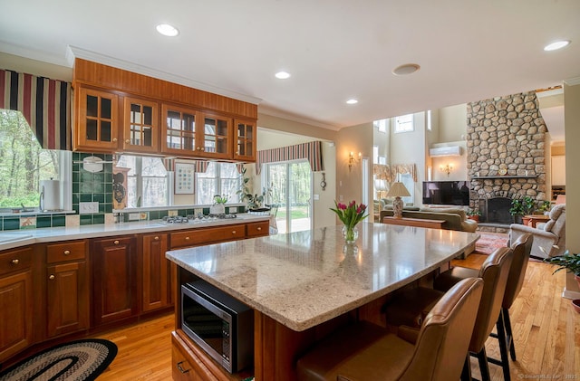 kitchen featuring light wood-style flooring, brown cabinetry, white gas cooktop, stainless steel microwave, and a kitchen island