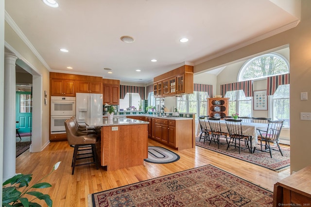 kitchen featuring a center island, glass insert cabinets, white appliances, crown molding, and brown cabinets