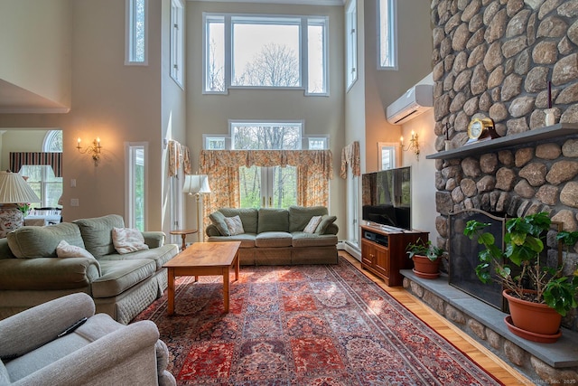 living room with a stone fireplace, a wall unit AC, light wood-type flooring, and a high ceiling