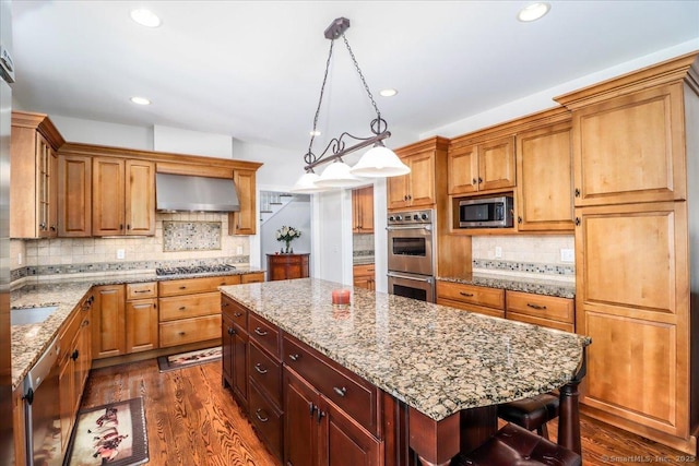 kitchen featuring decorative backsplash, a kitchen island, dark wood-type flooring, wall chimney exhaust hood, and stainless steel appliances