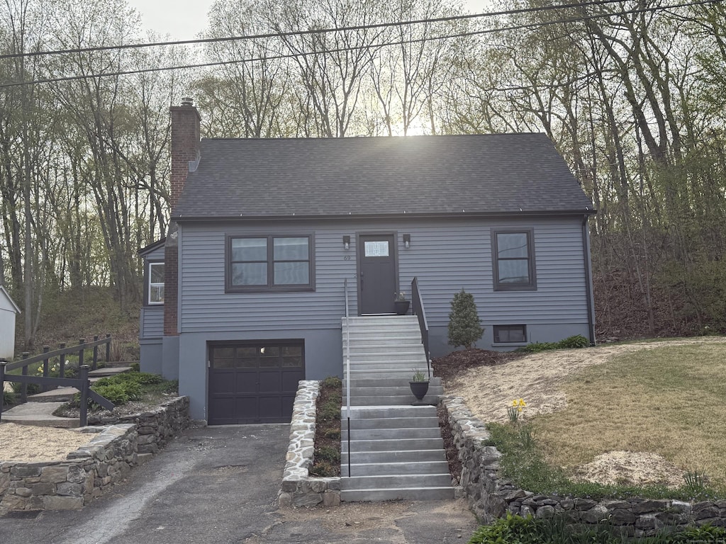 view of front of home featuring aphalt driveway, roof with shingles, a chimney, an attached garage, and stairway