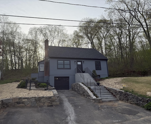 view of front facade featuring an attached garage, stairway, aphalt driveway, and a chimney