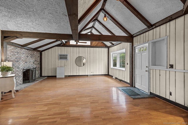 unfurnished living room with light wood finished floors, a wall unit AC, a brick fireplace, and a skylight
