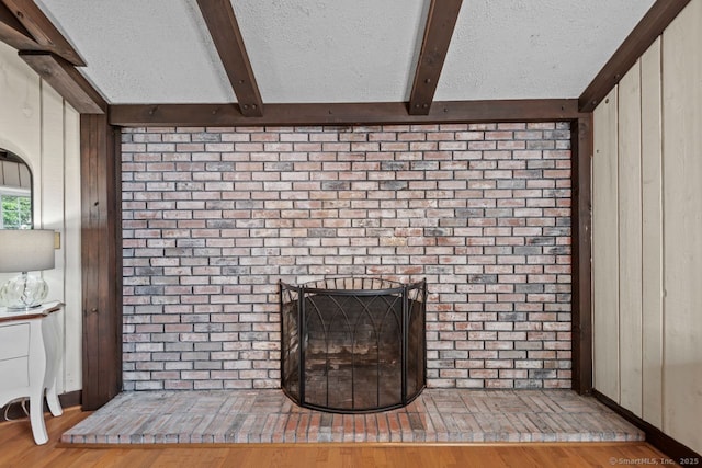 detailed view of beamed ceiling, wood finished floors, a textured ceiling, and a brick fireplace