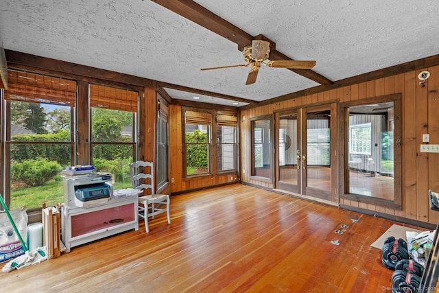 sunroom / solarium featuring wood walls, a textured ceiling, beam ceiling, wood finished floors, and a wooden deck