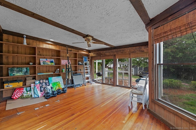 living area with wooden walls, wood-type flooring, a ceiling fan, beamed ceiling, and a textured ceiling