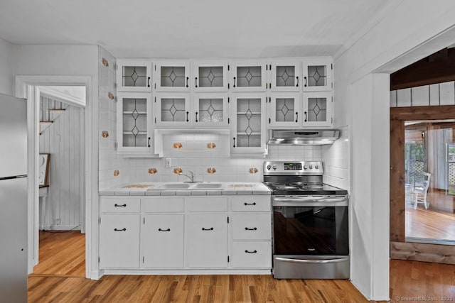 kitchen featuring appliances with stainless steel finishes, a sink, tile counters, under cabinet range hood, and decorative backsplash
