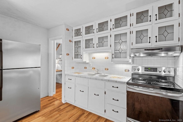 kitchen featuring appliances with stainless steel finishes, a sink, under cabinet range hood, light wood finished floors, and backsplash