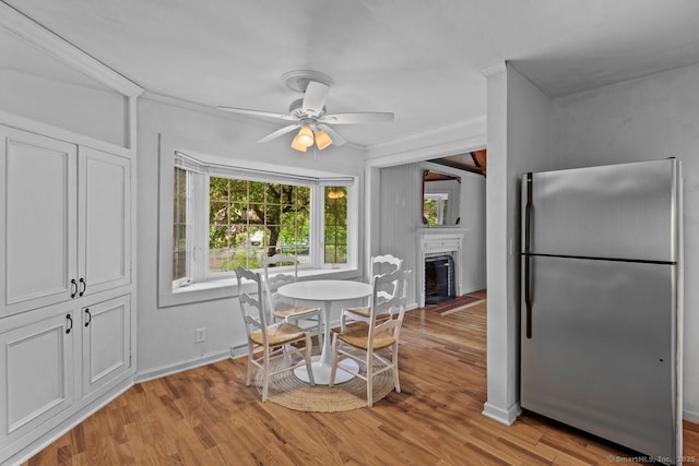dining area featuring a fireplace with flush hearth, light wood-style flooring, a ceiling fan, and baseboards