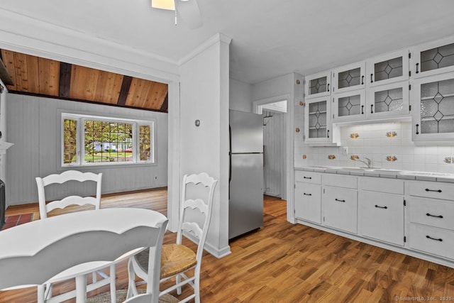 kitchen with freestanding refrigerator, a sink, decorative backsplash, tile countertops, and glass insert cabinets