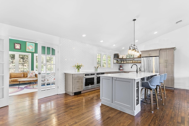kitchen featuring light countertops, a kitchen breakfast bar, gray cabinets, stainless steel appliances, and tasteful backsplash
