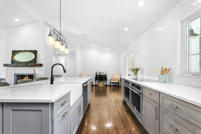 kitchen with gray cabinets, dark wood-style flooring, appliances with stainless steel finishes, a brick fireplace, and a sink