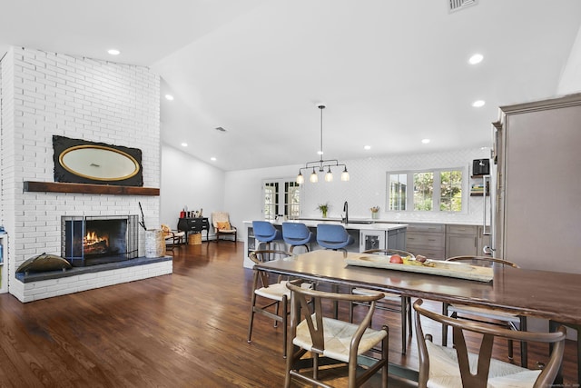 dining room with recessed lighting, a fireplace, vaulted ceiling, and dark wood-style flooring
