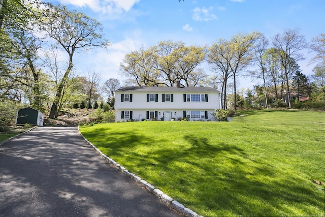 colonial home featuring a storage unit, an outdoor structure, a front lawn, and aphalt driveway