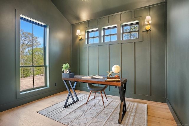 office with vaulted ceiling, a decorative wall, and light wood finished floors