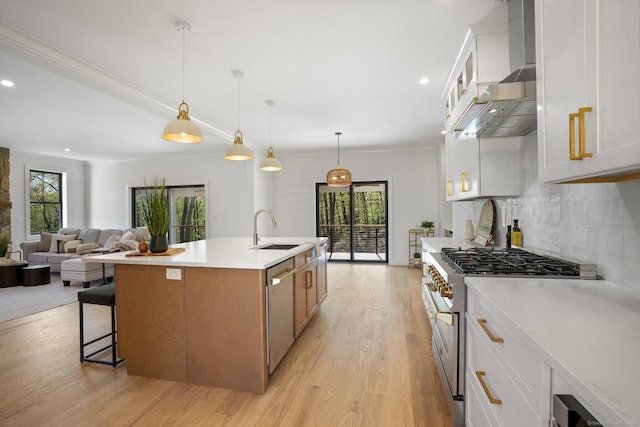 kitchen with wall chimney exhaust hood, a sink, light countertops, stainless steel appliances, and light wood-style flooring