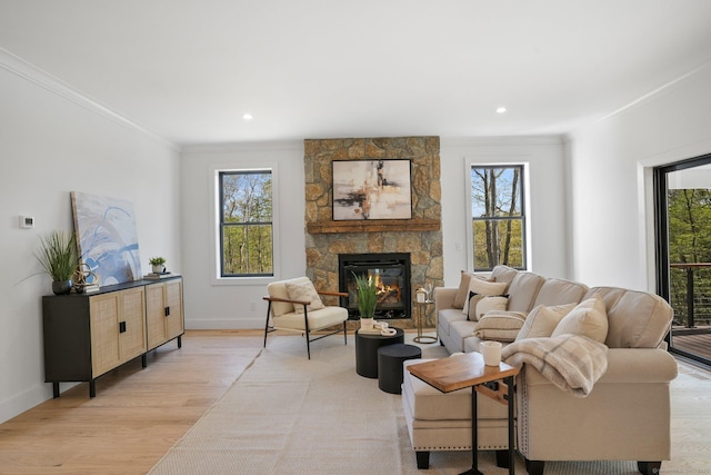 living room with a stone fireplace, crown molding, baseboards, light wood-style floors, and recessed lighting