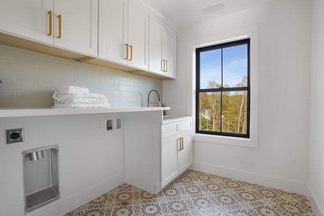 washroom with baseboards, hookup for an electric dryer, a sink, and cabinet space