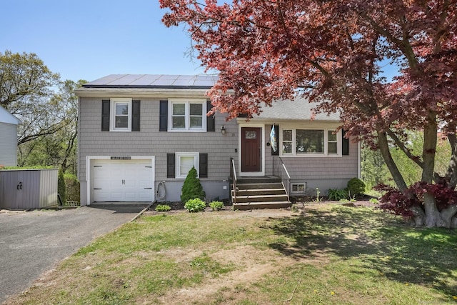 tri-level home featuring an attached garage, driveway, solar panels, and a front lawn