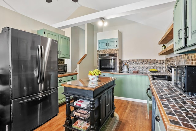 kitchen with a sink, appliances with stainless steel finishes, tile counters, and light wood-style floors