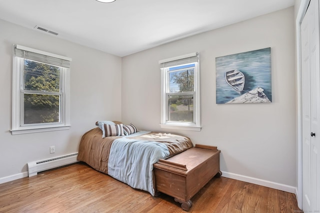 bedroom featuring visible vents, a baseboard radiator, light wood-style flooring, and baseboards