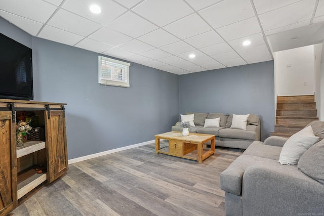 living area featuring stairs, wood finished floors, baseboards, recessed lighting, and a paneled ceiling