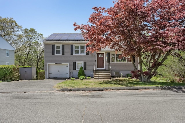 split level home with roof mounted solar panels, an attached garage, a front lawn, and aphalt driveway