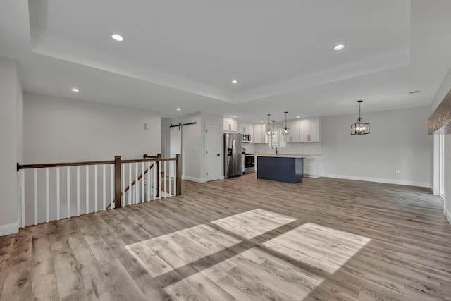 29 Sterling St, New Britain, CT 06053 - unfurnished living room featuring a barn door, a tray ceiling, recessed lighting, light wood-style flooring, and a chandelier