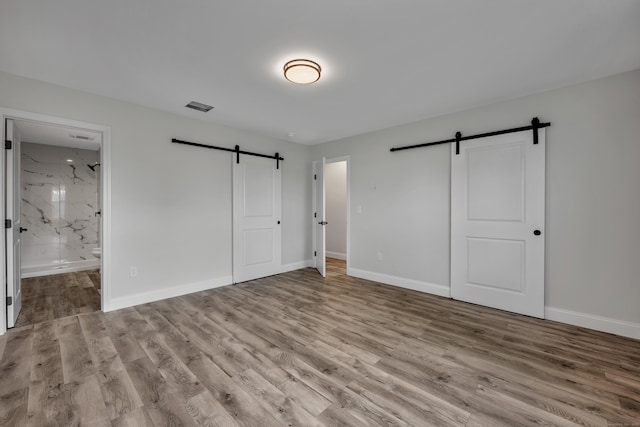 29 Sterling St, New Britain, CT 06053 - unfurnished bedroom featuring a barn door, wood finished floors, baseboards, and ensuite bath