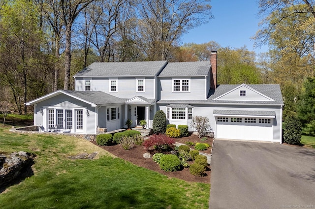 traditional-style home featuring roof with shingles, an attached garage, a front lawn, aphalt driveway, and a chimney