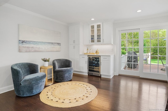 sitting room with crown molding, beverage cooler, dark wood finished floors, baseboards, and a bar