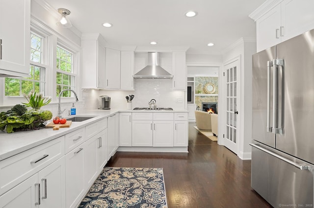 kitchen featuring high end fridge, gas cooktop, wall chimney exhaust hood, tasteful backsplash, and a sink