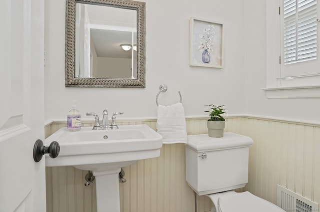 half bath featuring toilet, visible vents, and wainscoting