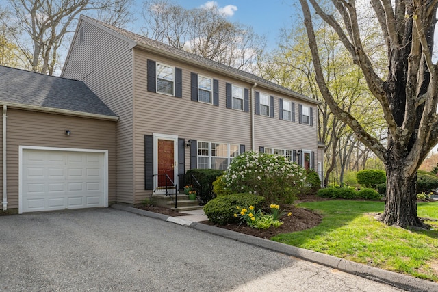 colonial home featuring a garage, a shingled roof, driveway, and a front yard