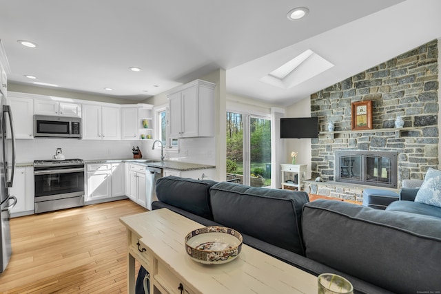 living area featuring light wood-type flooring, recessed lighting, vaulted ceiling with skylight, and a fireplace