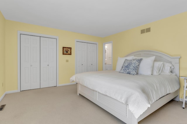 bedroom with baseboards, two closets, light colored carpet, and visible vents