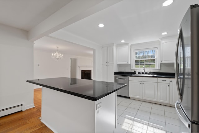 kitchen with dark countertops, baseboard heating, white cabinetry, a sink, and appliances with stainless steel finishes