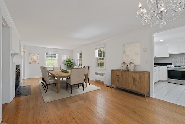 dining space featuring radiator, ornamental molding, light wood finished floors, and a notable chandelier