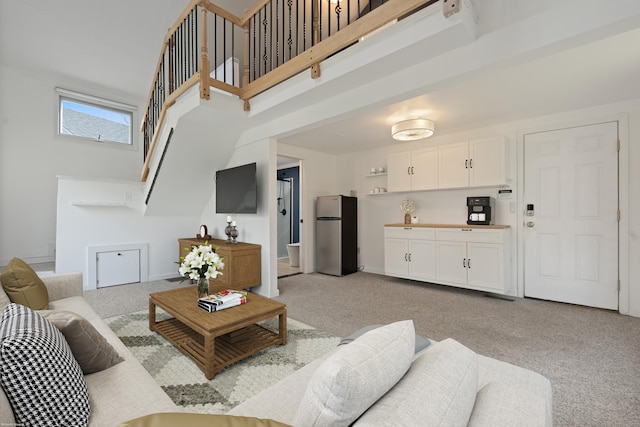 living area featuring stairs, light carpet, and a towering ceiling