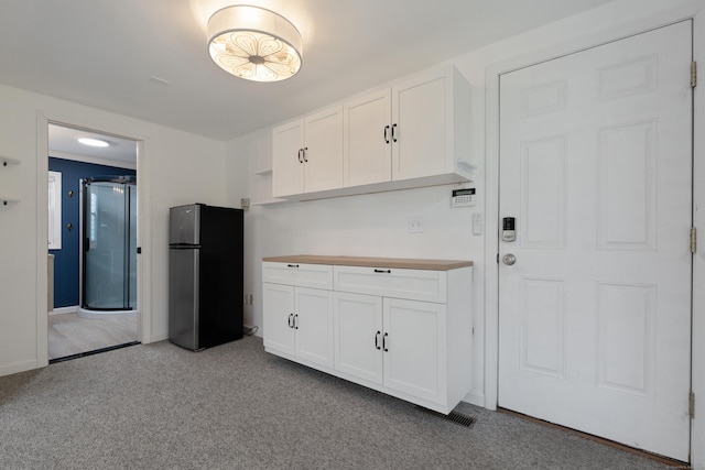 kitchen featuring freestanding refrigerator, white cabinets, wood counters, and carpet floors