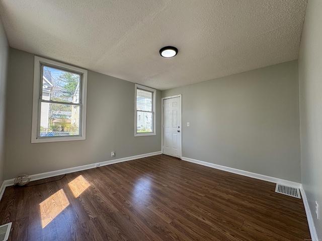 empty room with baseboards, a textured ceiling, dark wood-style flooring, and a healthy amount of sunlight