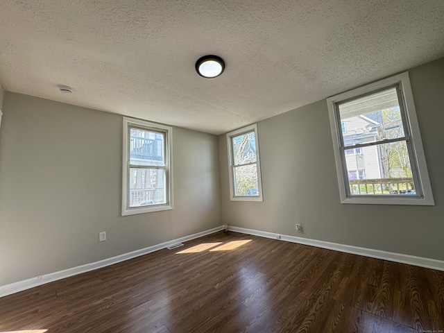 empty room with a textured ceiling, dark wood finished floors, baseboards, and visible vents