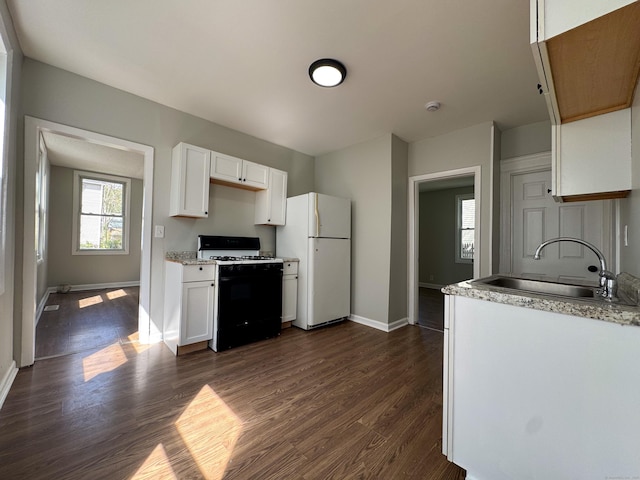 kitchen with a sink, baseboards, range with gas cooktop, and freestanding refrigerator