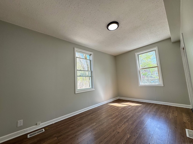 spare room with dark wood-style flooring, a textured ceiling, visible vents, and plenty of natural light