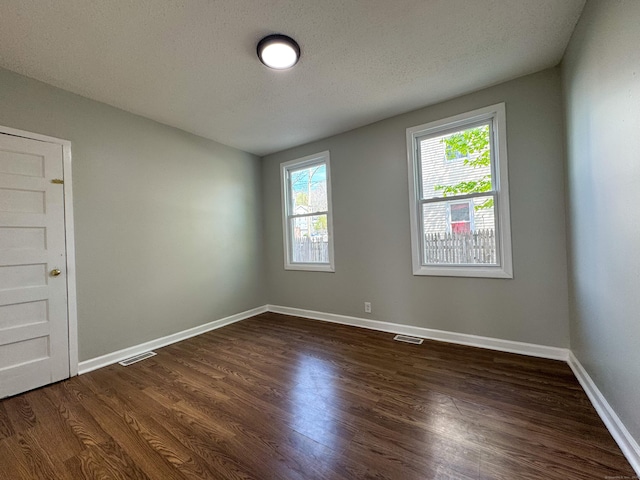 spare room featuring visible vents, a textured ceiling, baseboards, and dark wood-style floors